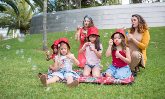 Group of children and adults blowing bubbles in a sunny park setting.