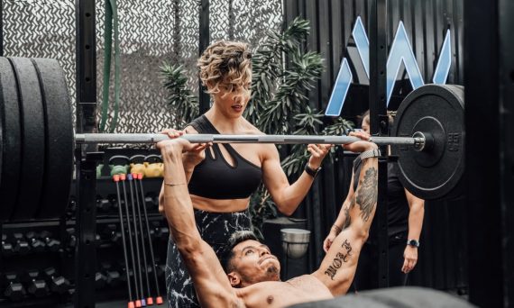 Man lifting weights with woman spotting in Mexico City gym. Urban and dynamic fitness scene.